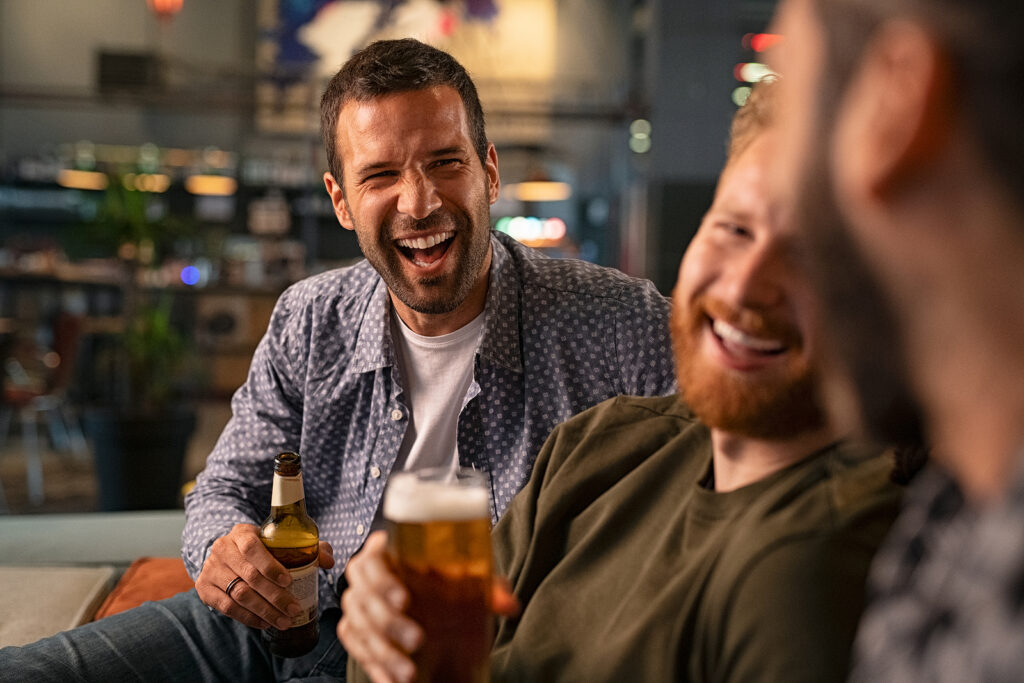 Happy young men drinking beer while having fun in a pub