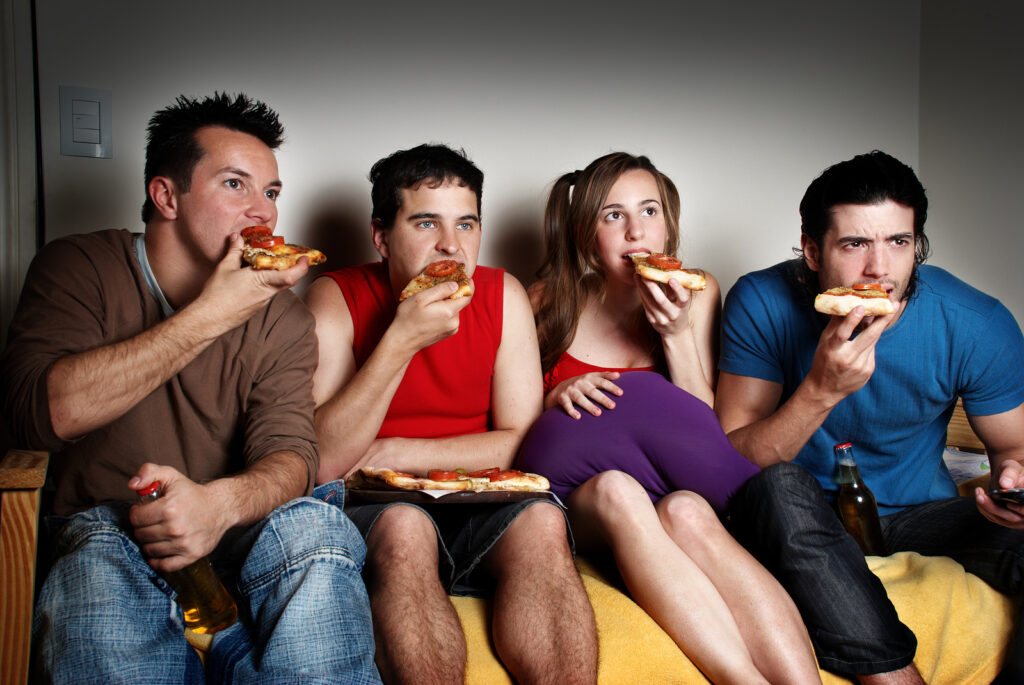 Four concentrated fans with a pizza in hands, watching TV