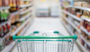 Blurred effect in the Supermarket aisle with empty silver and green shopping trolley.