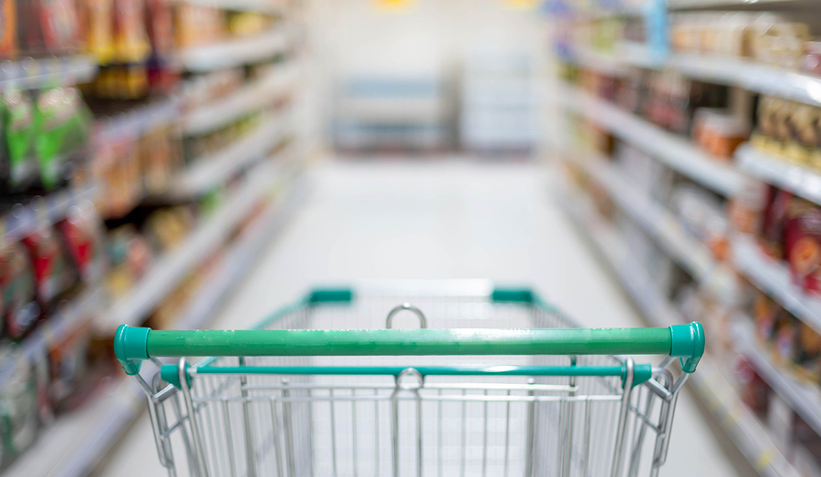 Blurred effect in the Supermarket aisle with empty silver and green shopping trolley.